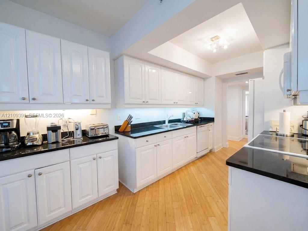 Kitchen featuring white cabinetry, dark stone countertops, wood-finish flooring, dual-basin stainless steel sink, and flush-mount ceiling lighting