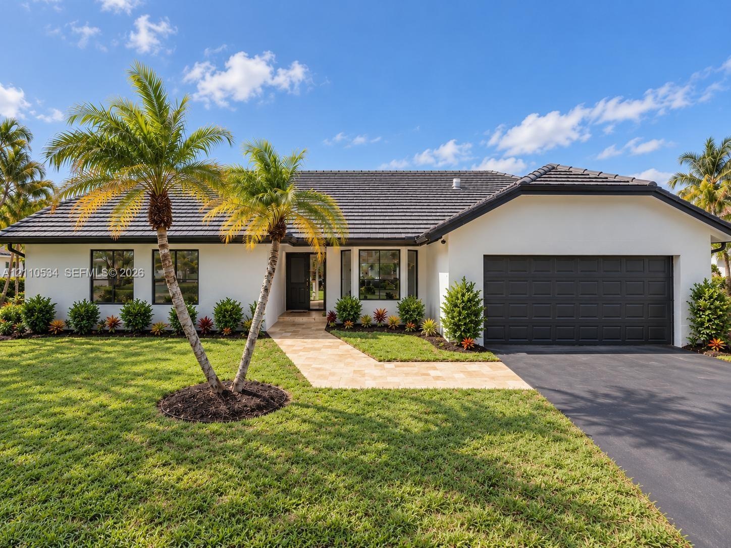 Single-story exterior featuring white stucco siding, a charcoal tile roof, a multi-paneled garage door, and a stone-paver walkway