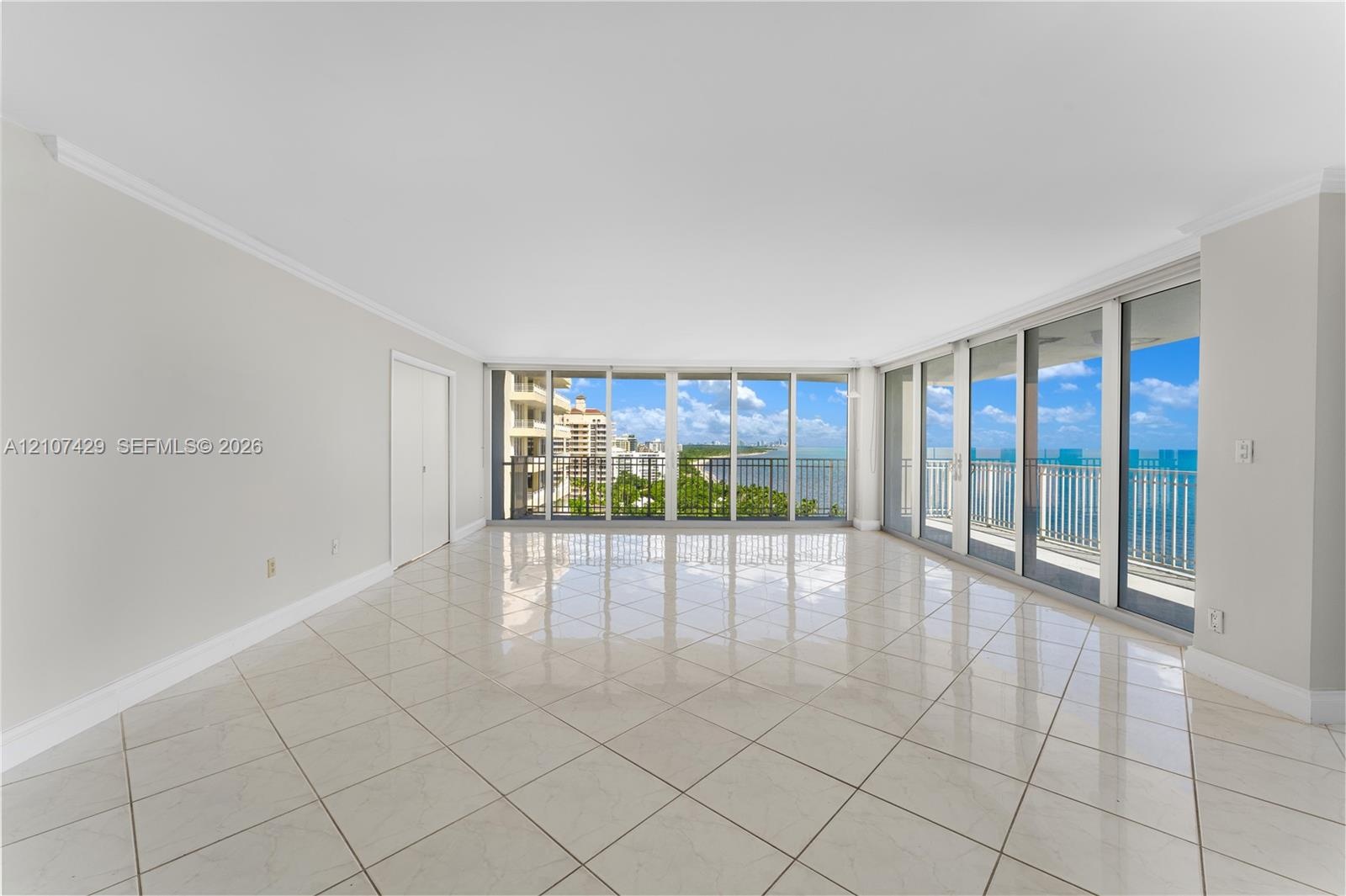 Expansive interior space featuring large-format tile flooring, crown molding, and floor-to-ceiling glass panel walls with access to a balcony