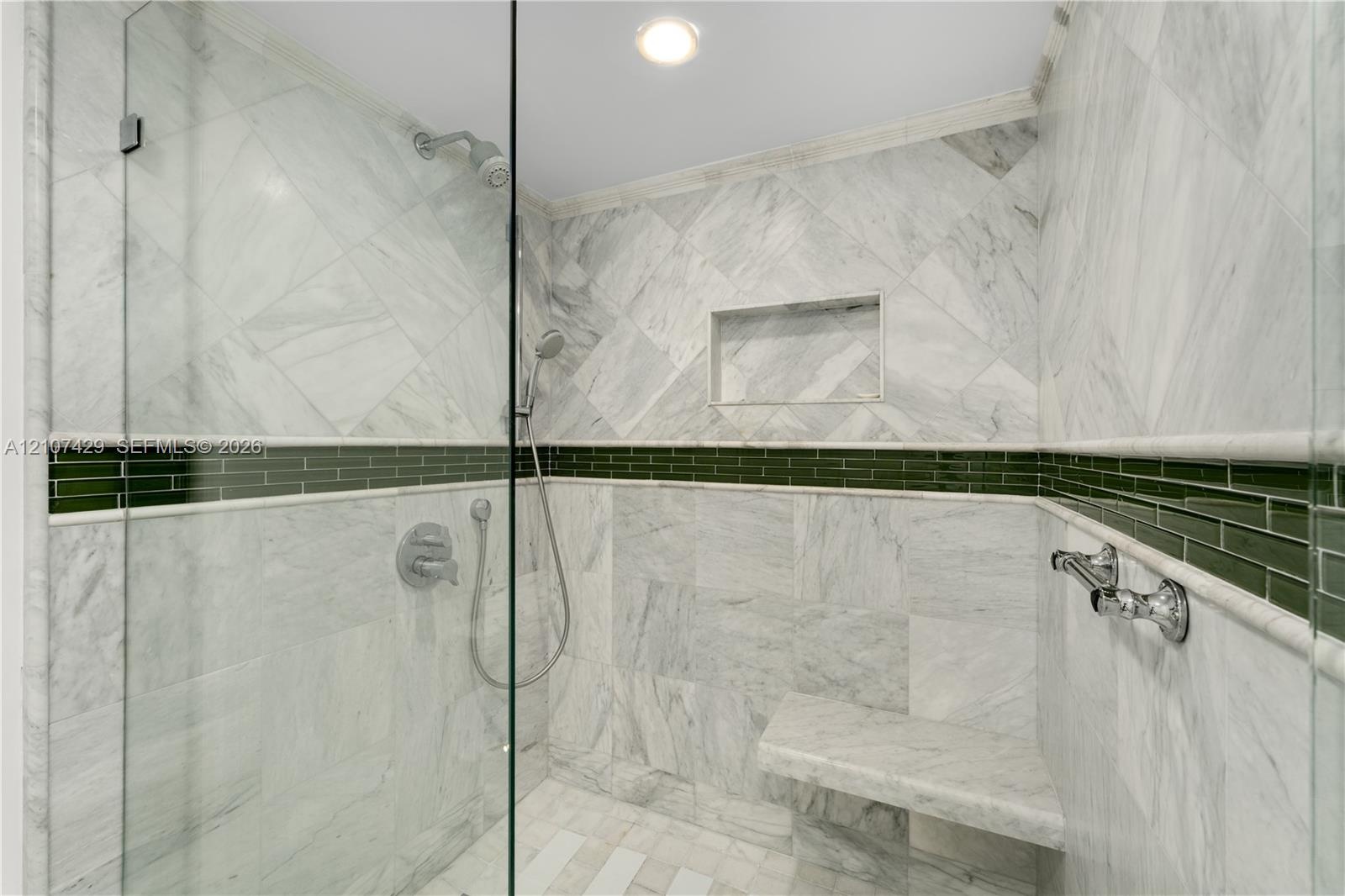 Walk-in shower featuring large-format stone tile, a built-in bench, a glass enclosure, an integrated wall niche, and a contrasting green glass tile ac
