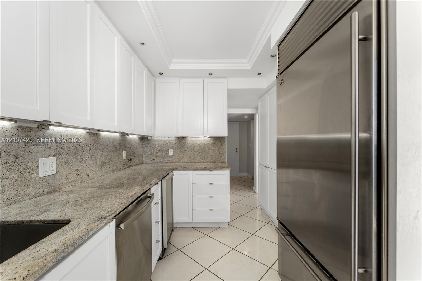 Kitchen featuring white shaker-style cabinetry, stone countertops, stainless steel appliances, under-cabinet lighting, and tile flooring