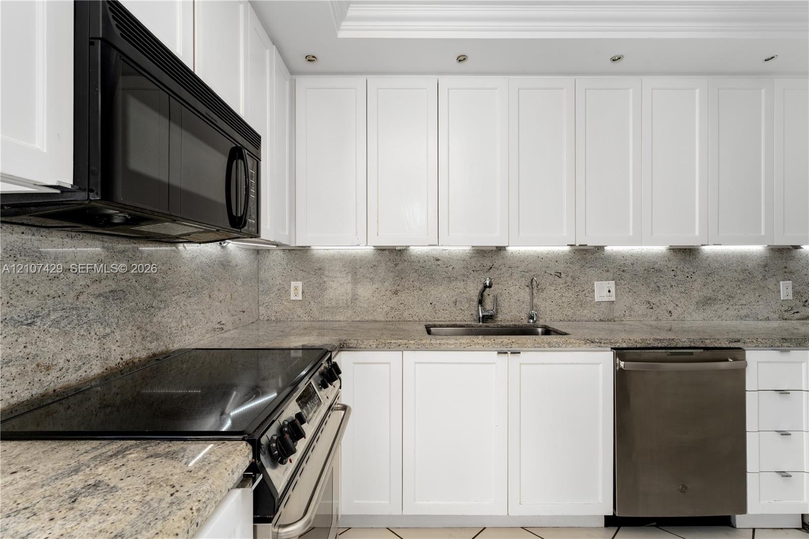 White shaker-style cabinetry, stone countertops with matching full-height backsplash, undermount sink with arched faucet, stainless steel appliances, 