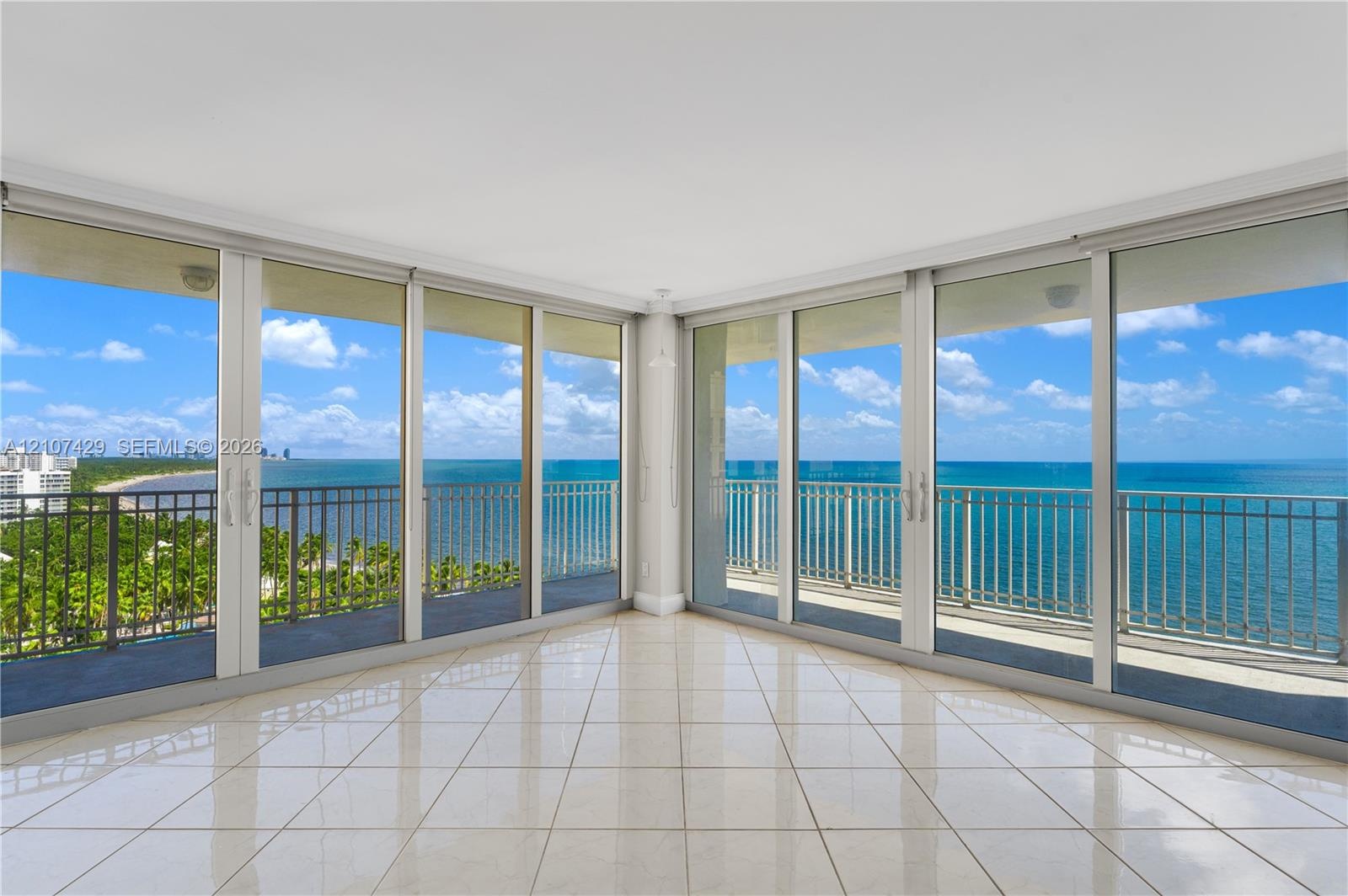 Floor-to-ceiling glass panel walls, wraparound balcony with metal railing, and light-toned ceramic tile flooring