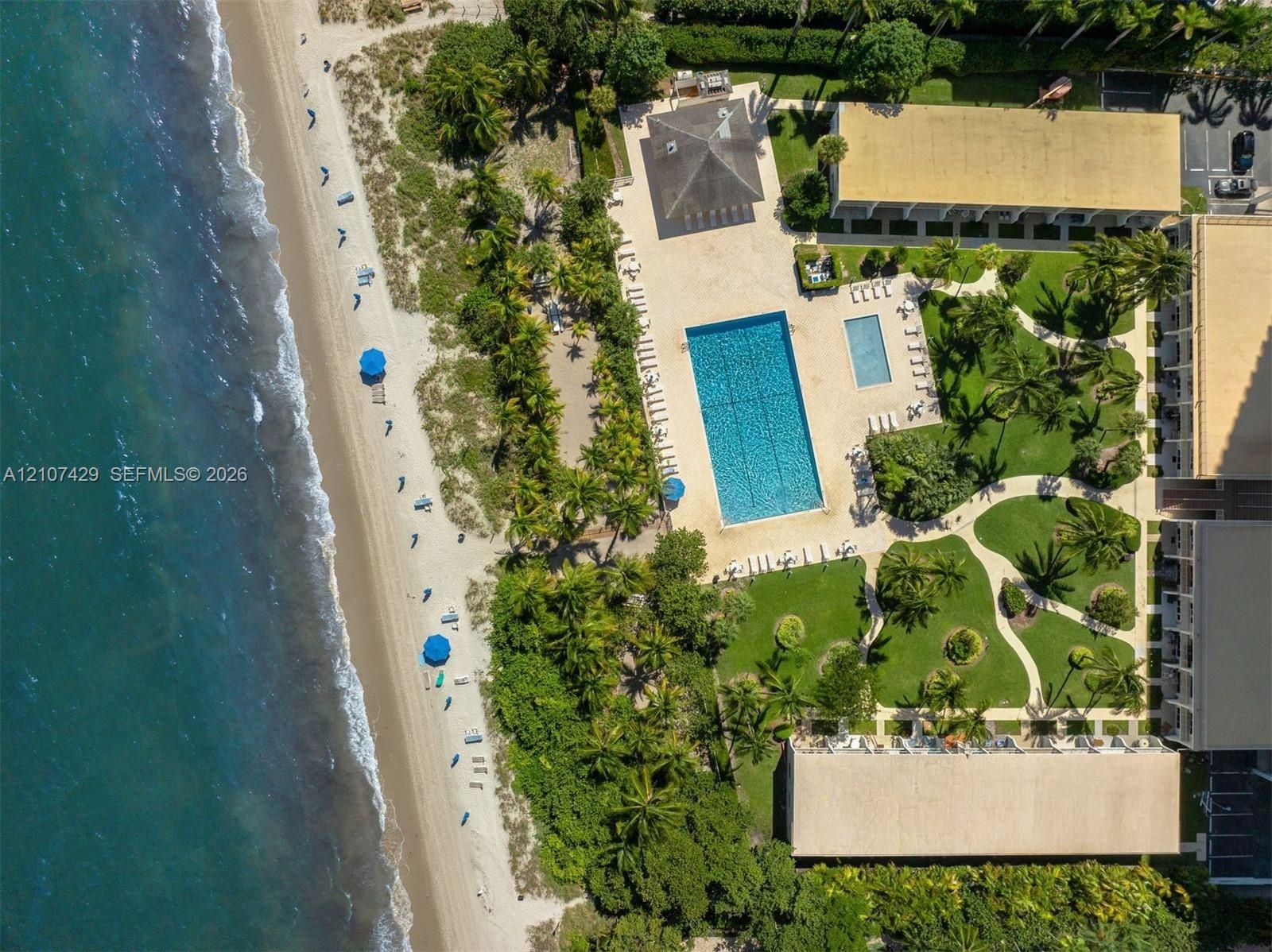 Oceanfront property featuring direct beach access, an expansive rectangular swimming pool, a separate secondary pool, manicured lawns, and established