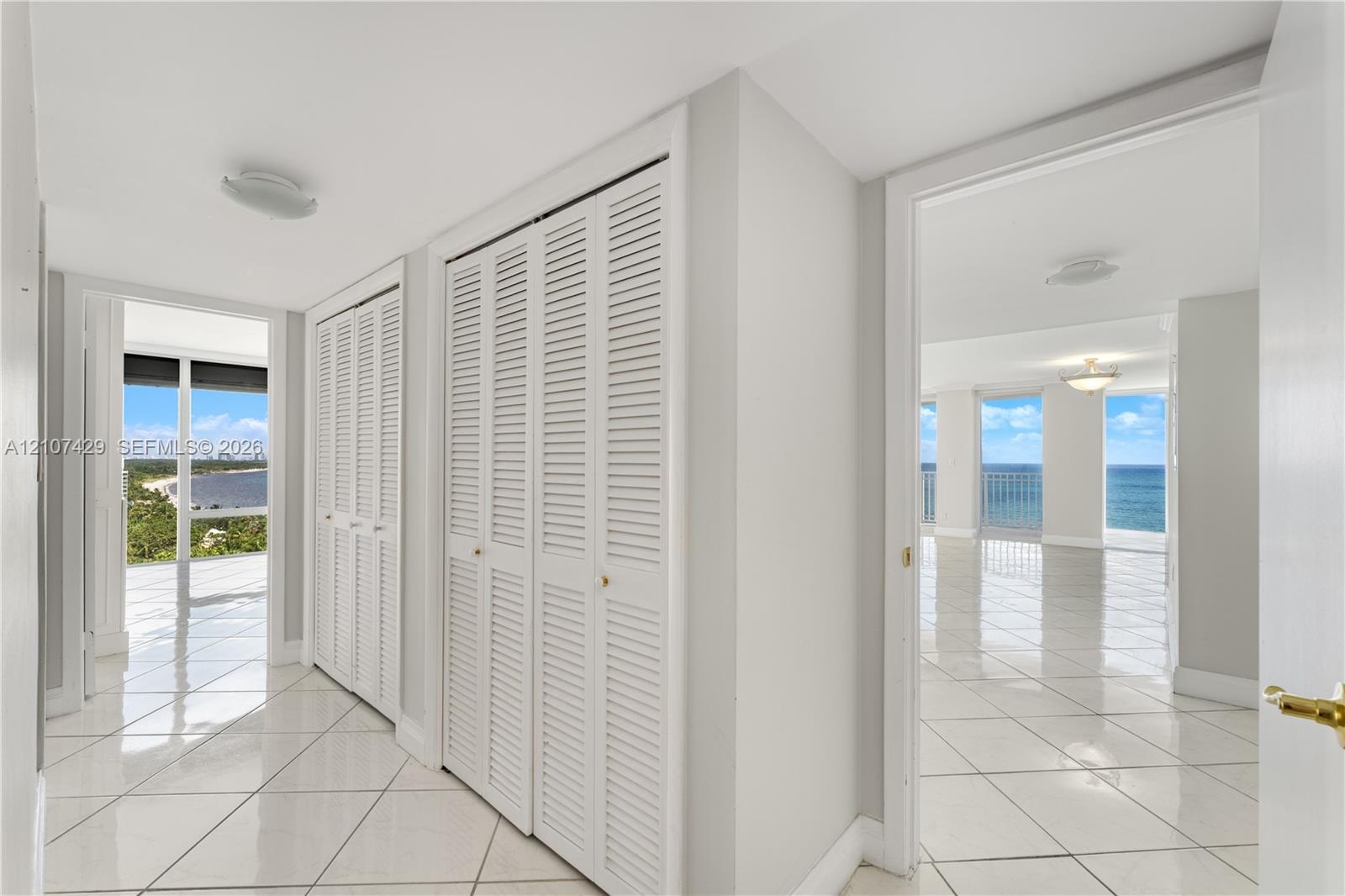 Interior hall featuring white tile flooring, floor-to-ceiling louvered closet doors, and multiple entryways showcasing direct water and shoreline scen