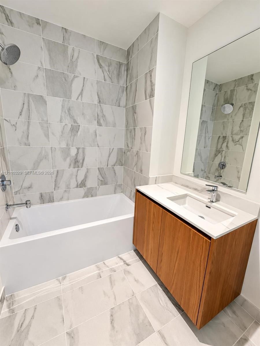 Bathroom featuring a wood-finish vanity with an integrated rectangular sink, stone-composite countertop, full-width wall mirror, and porcelain tile fl