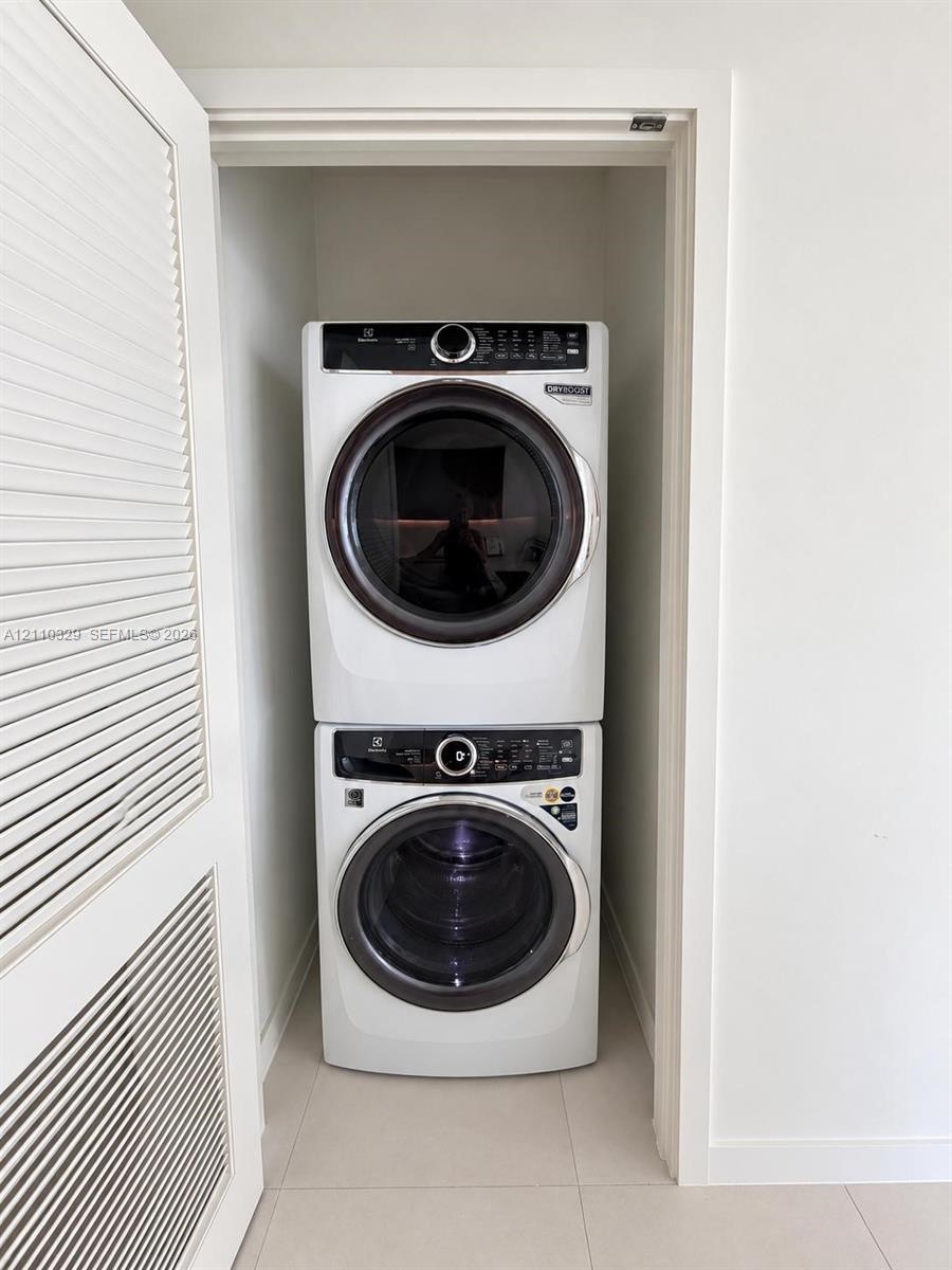 Stacked laundry center featuring a high-efficiency front-load washer and dryer set, housed within a closet with louvered bi-fold doors