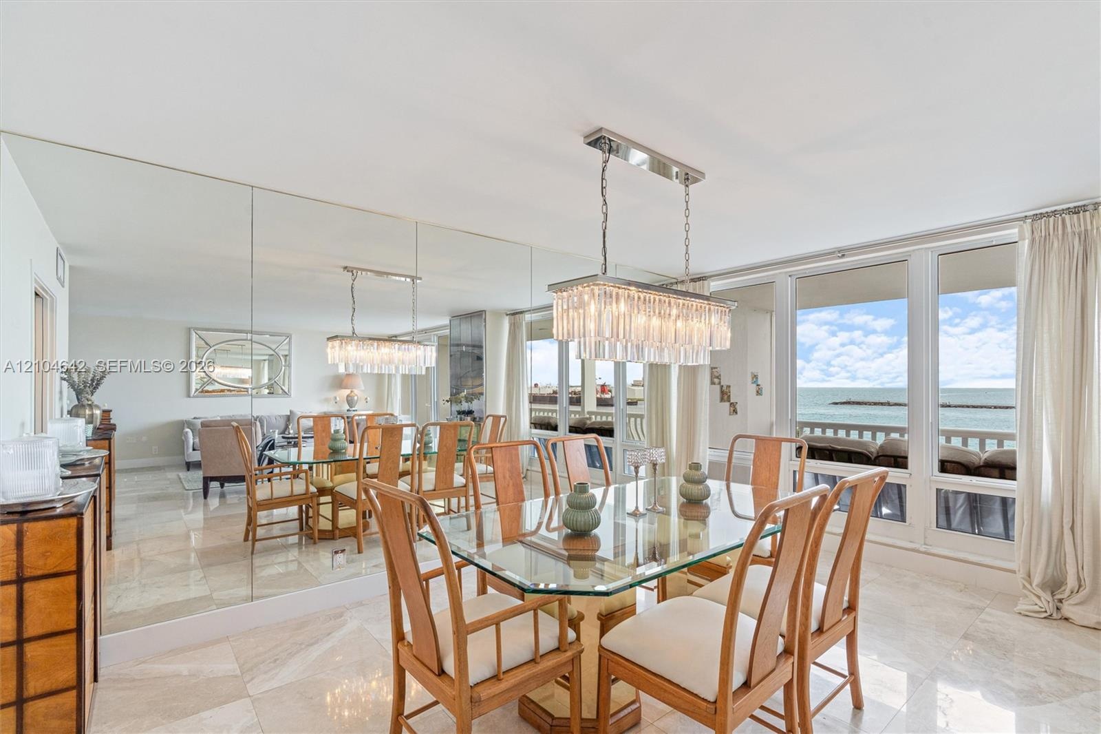Dining area featuring large-format stone tile flooring, floor-to-ceiling mirror wall, rectangular crystal chandelier, and sliding glass doors with dir
