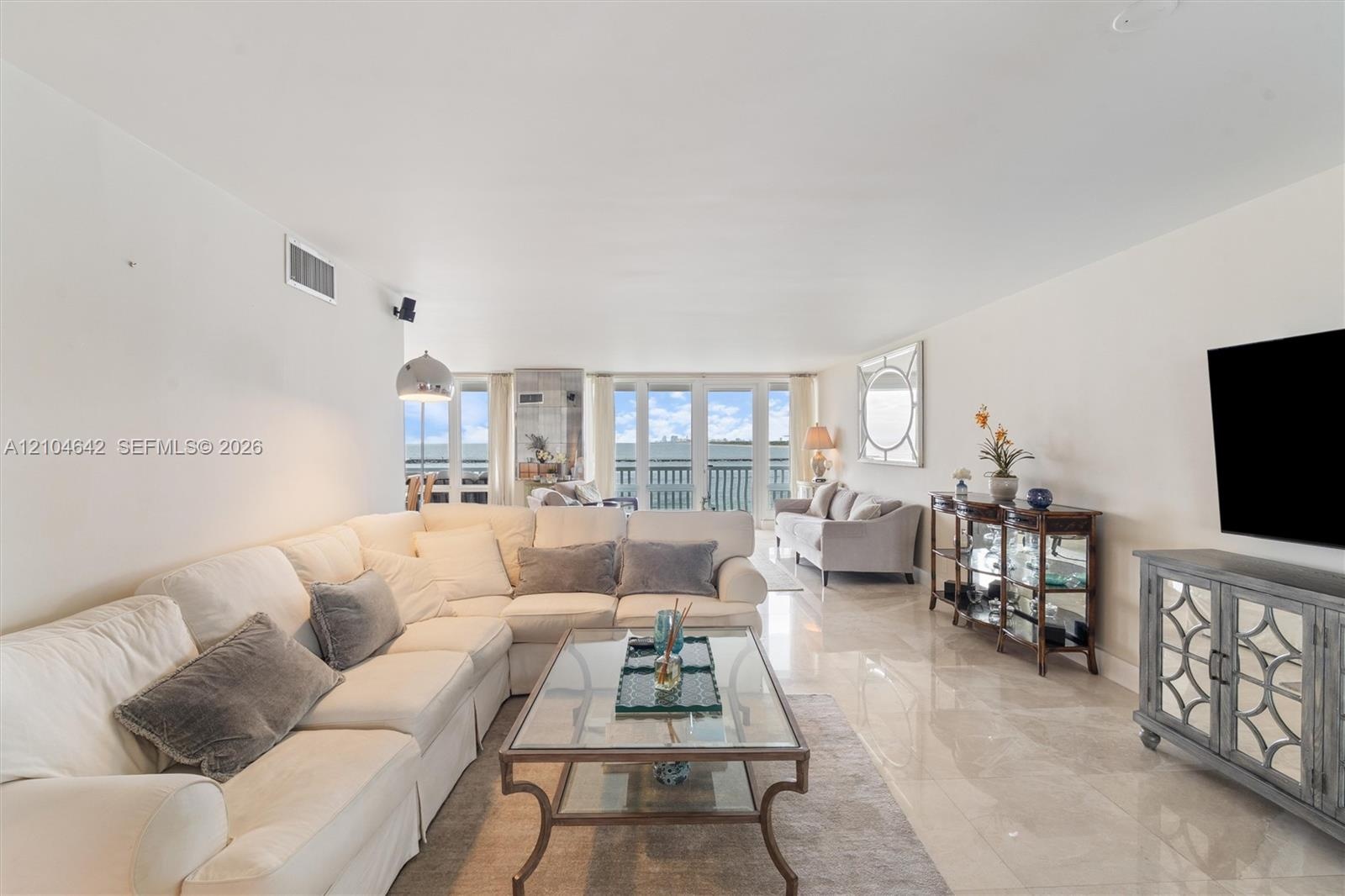 Living area featuring polished stone tile flooring, floor-to-ceiling glass panel doors, and a decorative wall-mounted mirror