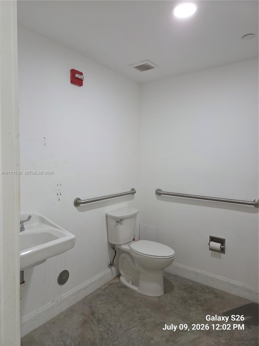 Wall-mounted porcelain sink with chrome faucet, floor-mounted toilet, and stainless steel grab bars