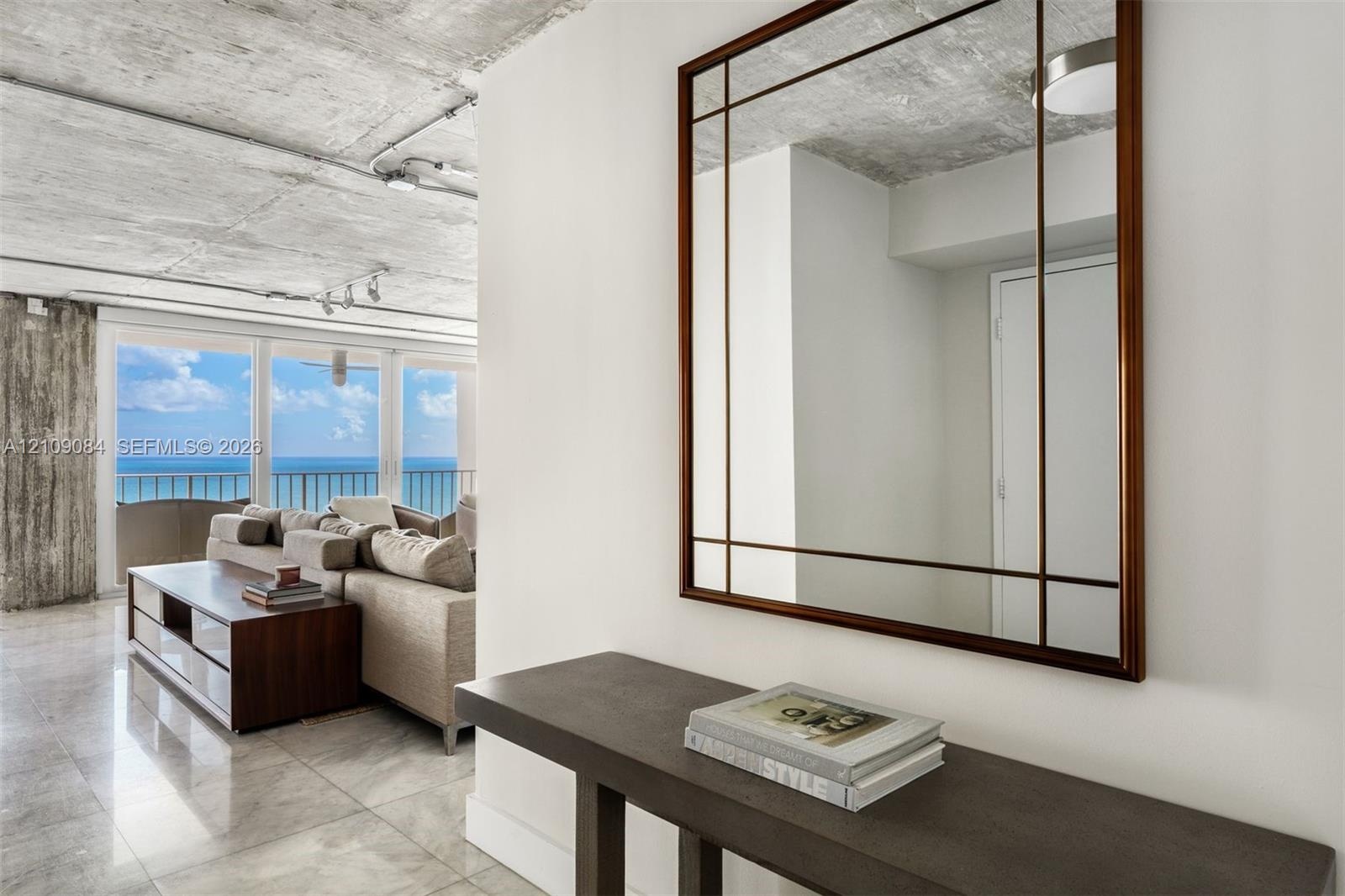 Exposed concrete ceiling, floor-to-ceiling glass paneling, stone-finish flooring, white flat-panel cabinetry, and a center island with a built-in wine