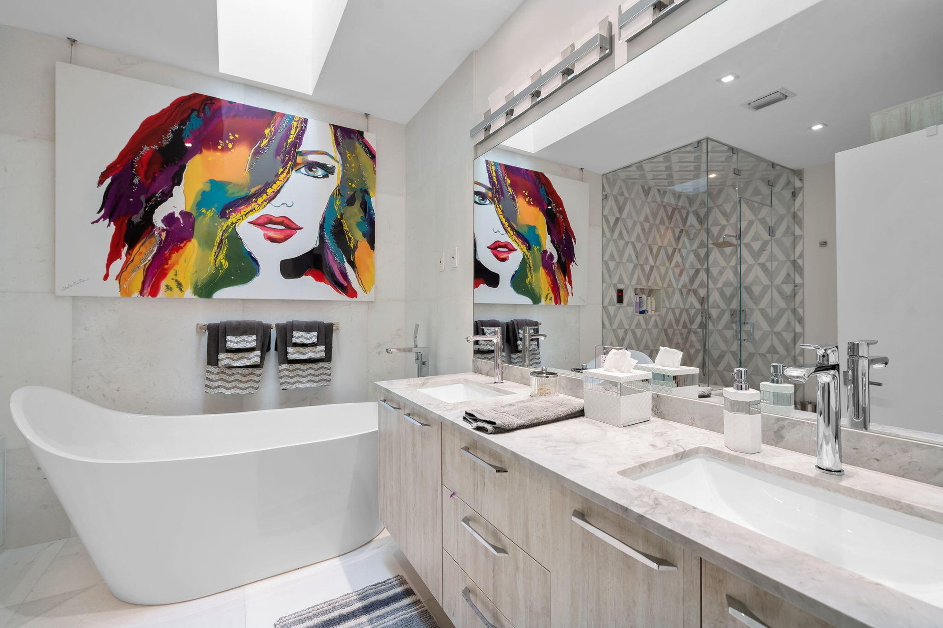 Skylight, freestanding soaking tub, double-sink vanity with stone countertop, walk-in glass-enclosed shower, and recessed ceiling lighting