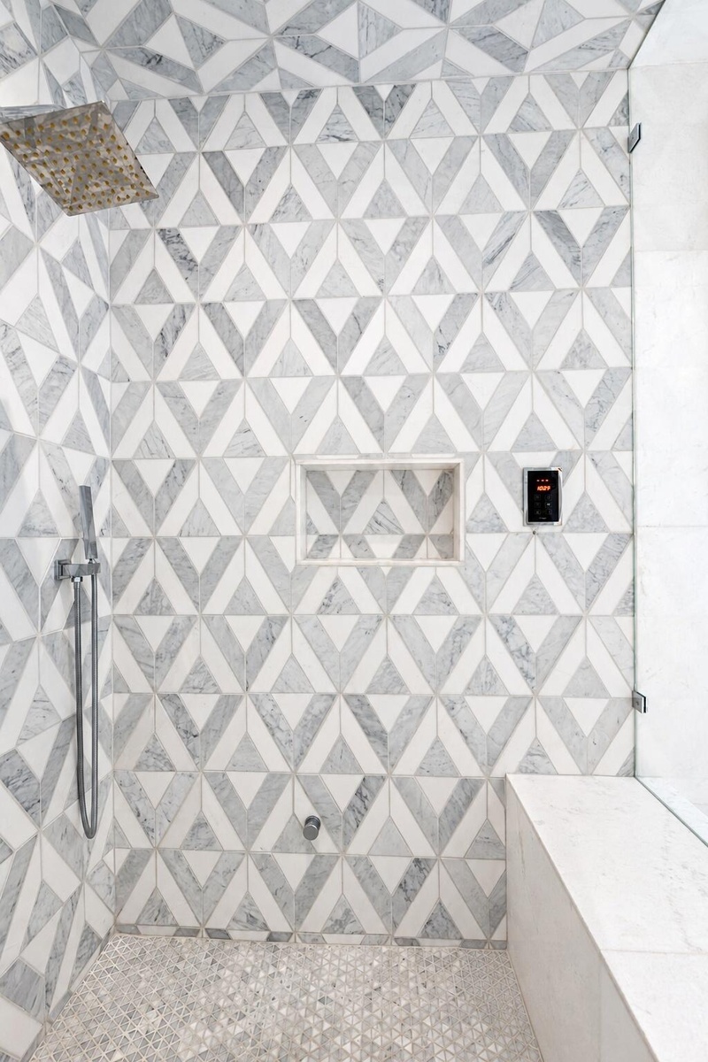 Glass enclosed walk in steam shower with geometric patterned tile and bench seating. Newly remodeled