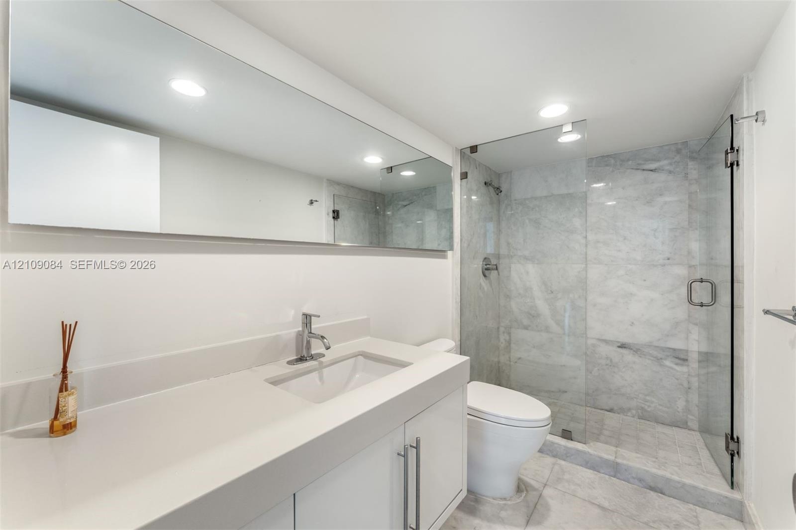 Exposed concrete ceiling with industrial-style track lighting, large-format tile flooring, and custom wall-mounted wood cabinetry with integrated shel