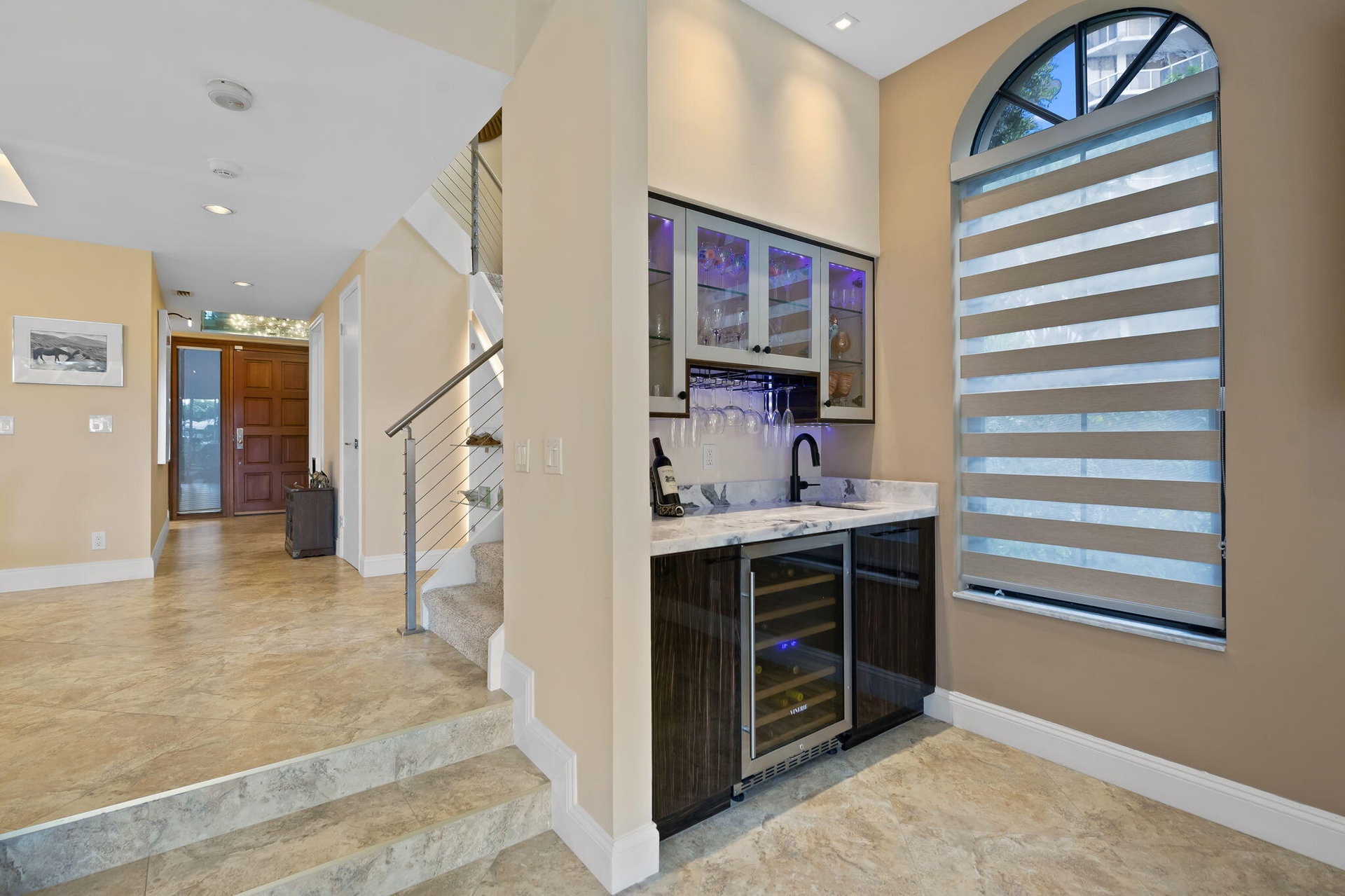 Built-in wet bar featuring dark wood-finish cabinetry, integrated wine refrigerator, stone countertop, and glass-front upper cabinets with accent ligh