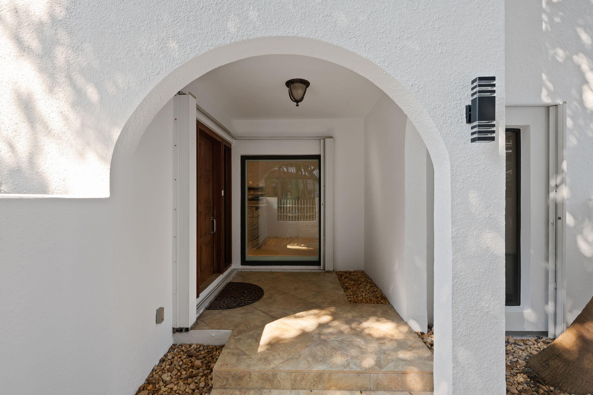 Covered entryway featuring a stucco arch, stone-tile flooring, wood-framed door, and modern rectangular wall-mounted lighting