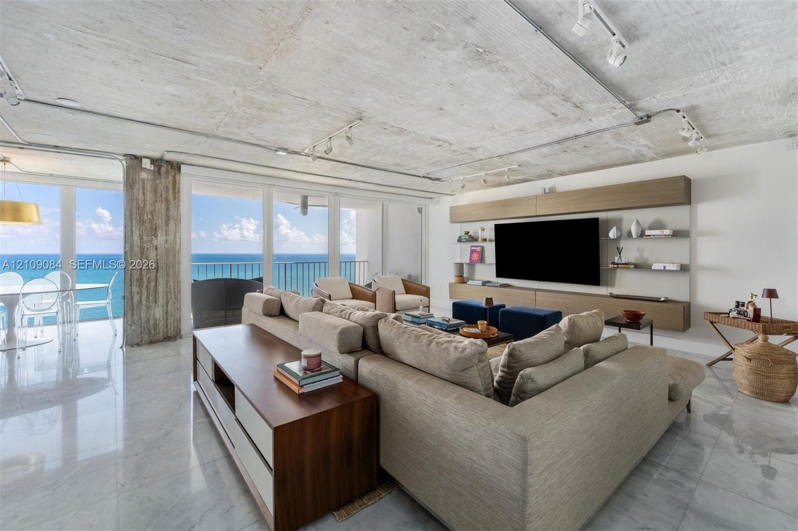 Contemporary kitchen featuring high-gloss white cabinetry, a waterfall-edge quartz island, stainless steel appliances, exposed concrete ceiling with i