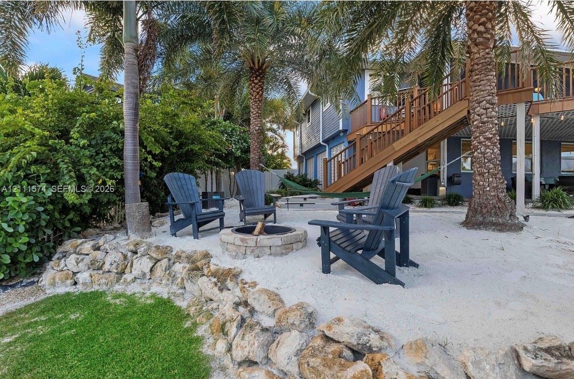 Backyard featuring a sand-ground fire pit, stacked stone retaining wall, mature palm trees, and a wooden exterior staircase