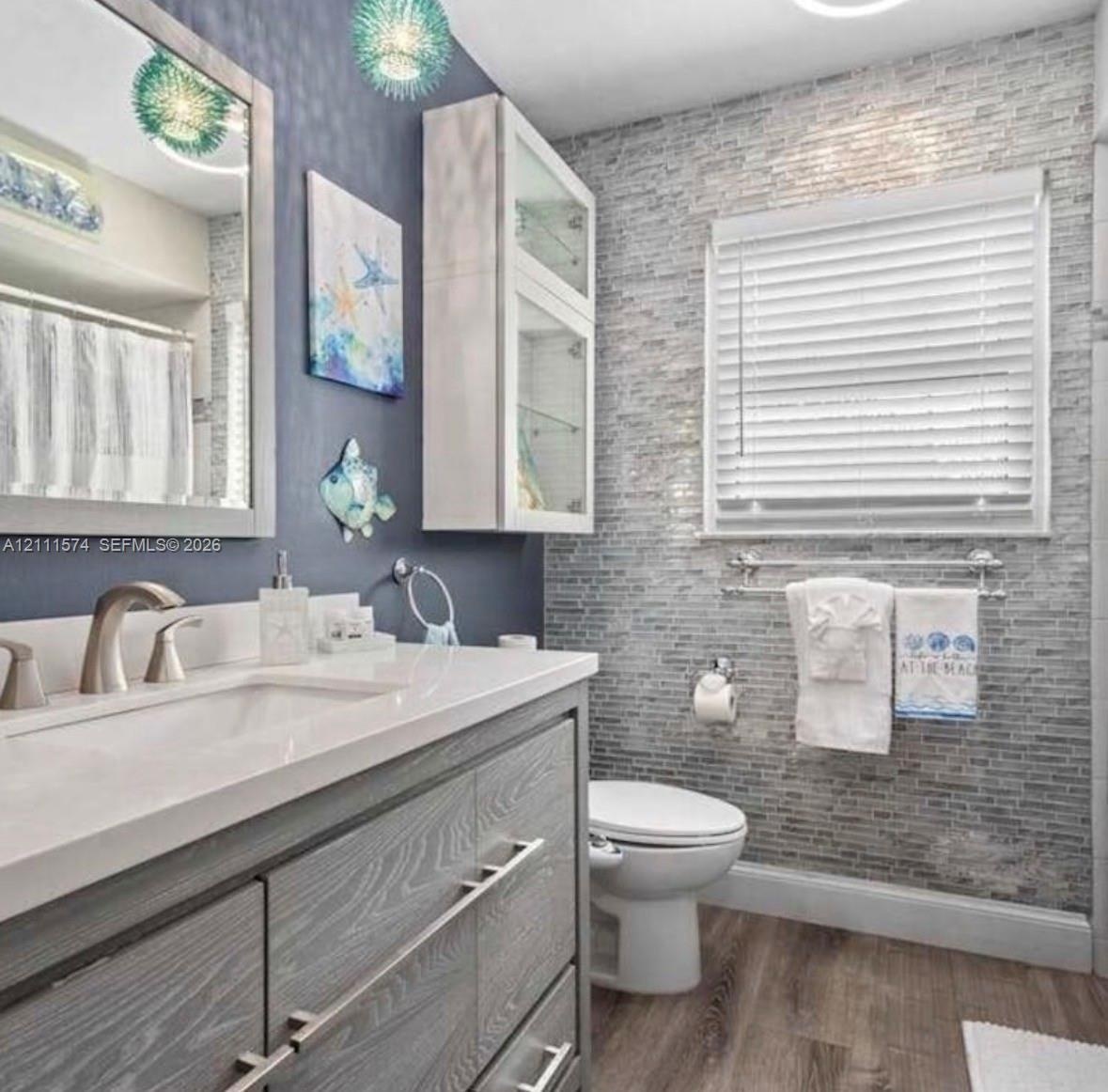 Vanity featuring a stone-finish countertop, undermount sink, and wood-finish cabinetry with brushed metal pulls