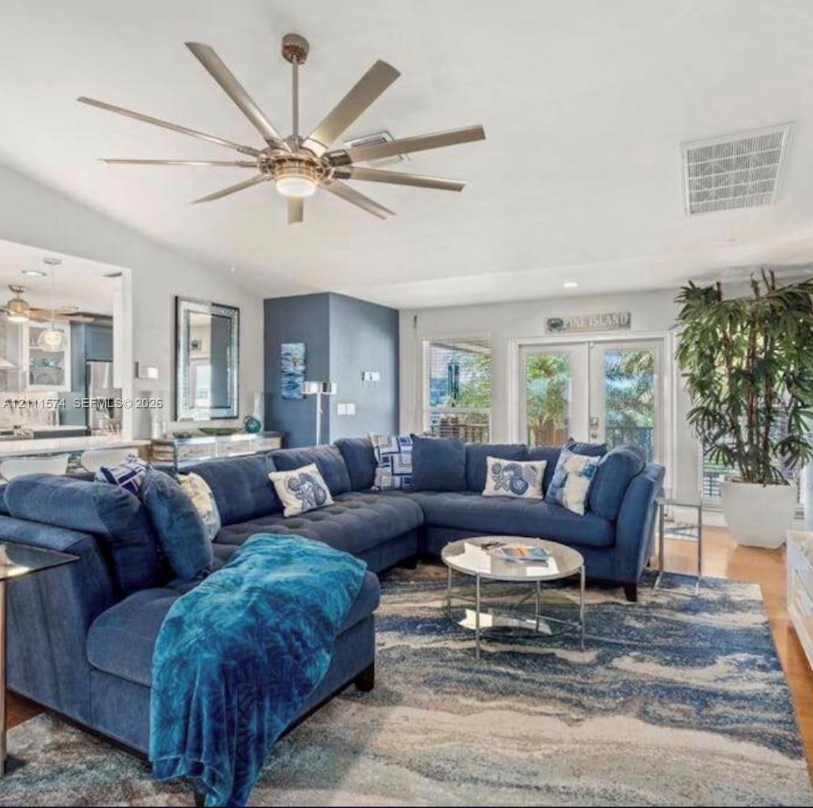 Multi-blade brushed-nickel ceiling fan with integrated center light, glass-paneled double doors, wood-finish flooring, and crisp white trim