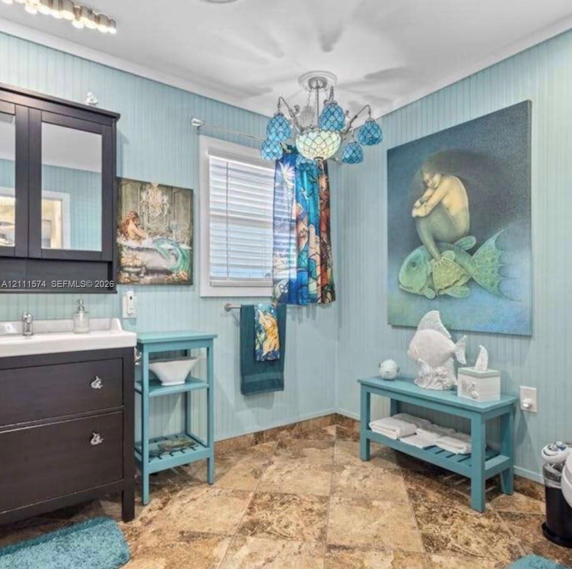 Bathroom featuring beadboard wall paneling, a dark wood-finish vanity with a rectangular sink, multi-tone tile flooring, and a decorative multi-arm ch