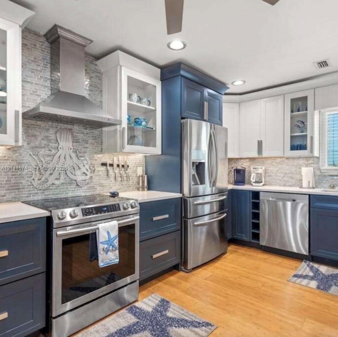 Kitchen featuring two-tone cabinetry, stainless steel appliances, a glass-tile backsplash with decorative accent, solid surface countertops, and wood-