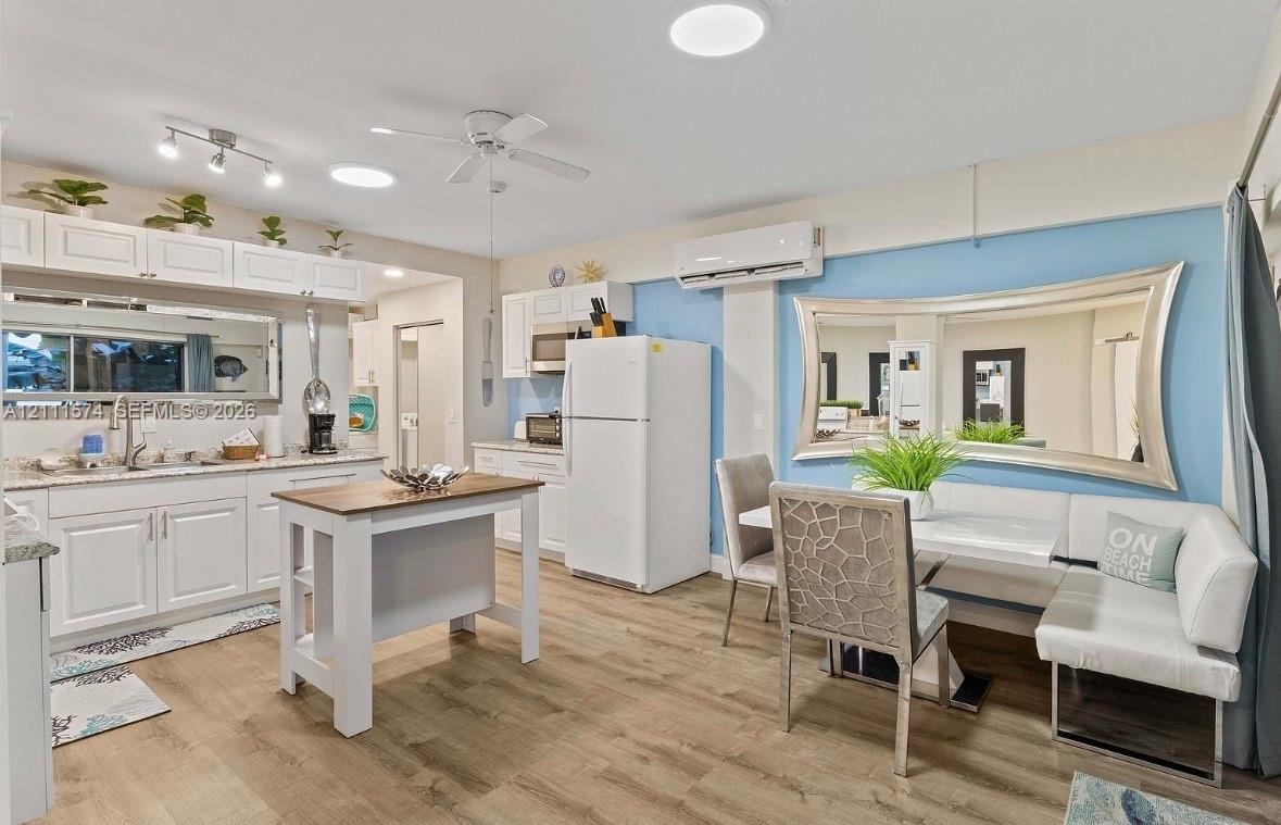Kitchen featuring white cabinetry, stone-finish countertops, wood-finish flooring, wall-mounted ductless air conditioning unit, and recessed lighting