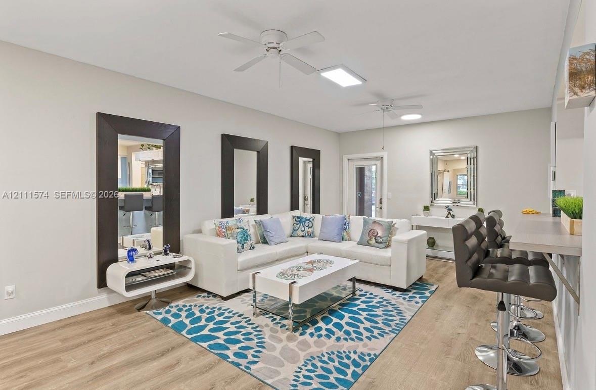 Living area featuring wood-finish flooring, two ceiling fans, recessed lighting, and three wall-mounted, dark-framed mirrors