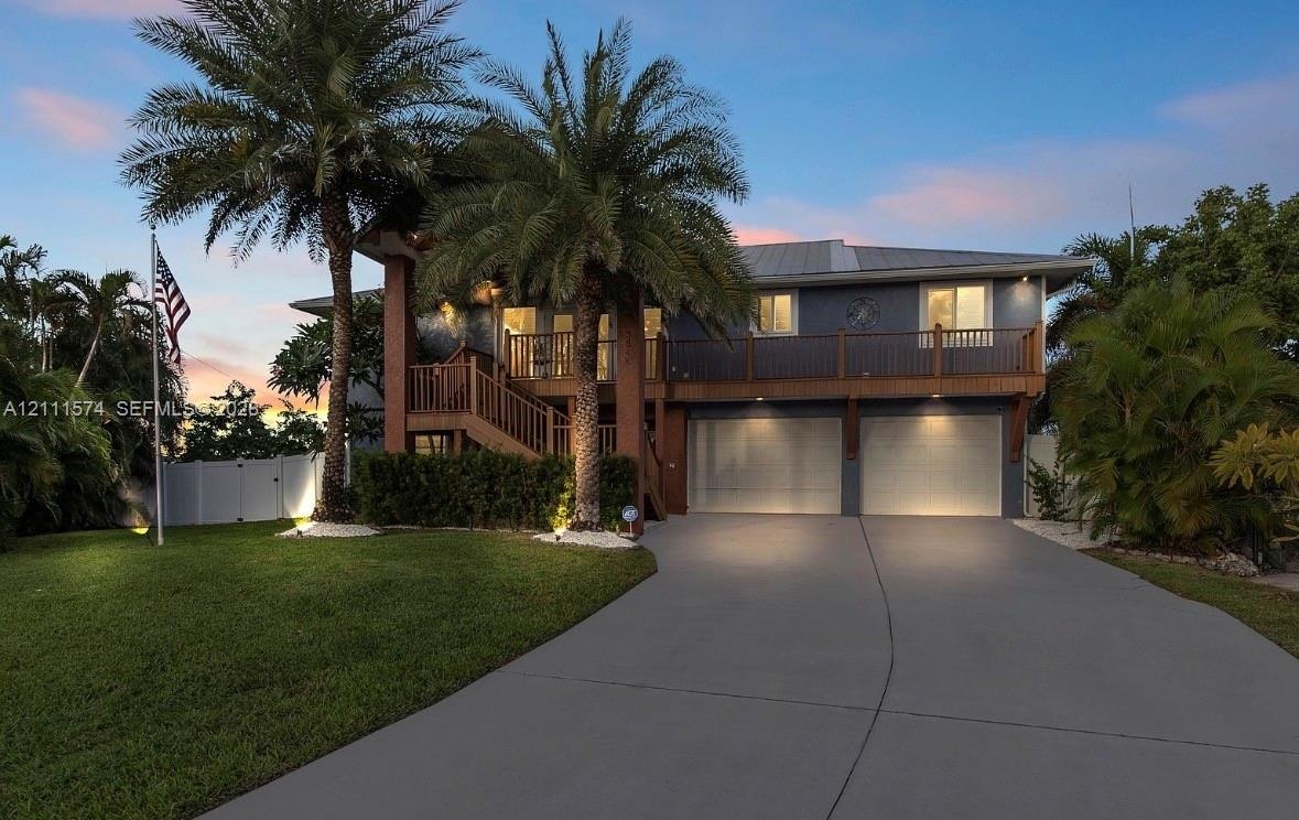 Two-story residence featuring a metal roof, attached two-car garage, elevated wooden staircase, wrap-around balcony with wooden railings, and mature p