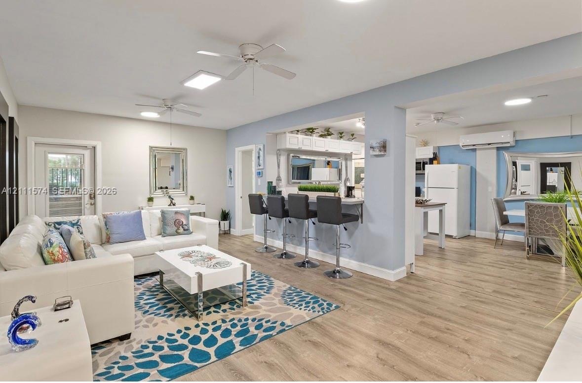 Open-concept interior featuring wood-finish flooring, a kitchen pass-through counter, ceiling fans, and a ductless mini-split system