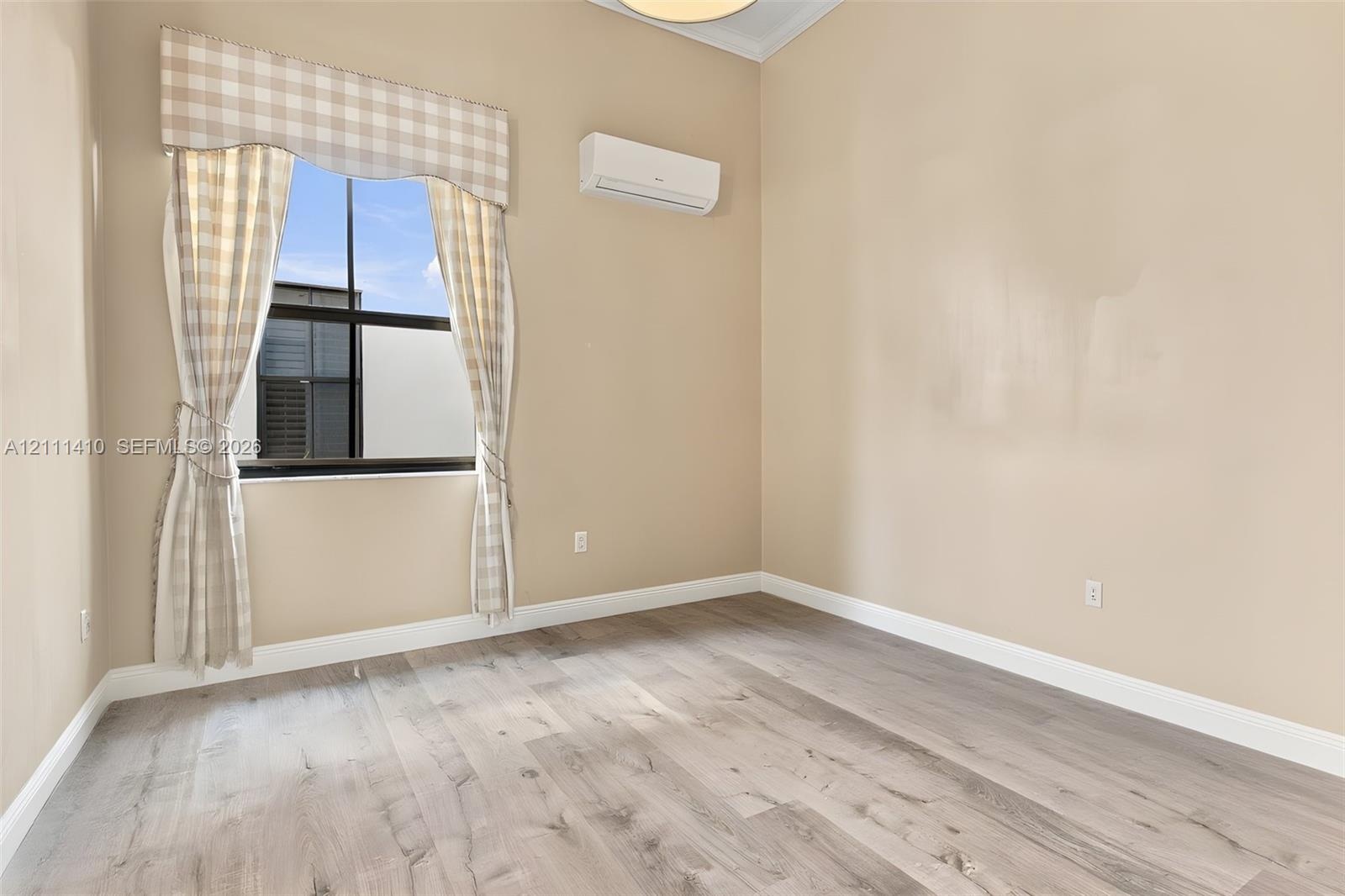 Room featuring wood-finish flooring, a wall-mounted ductless air conditioning unit, and a window with a dark metal frame