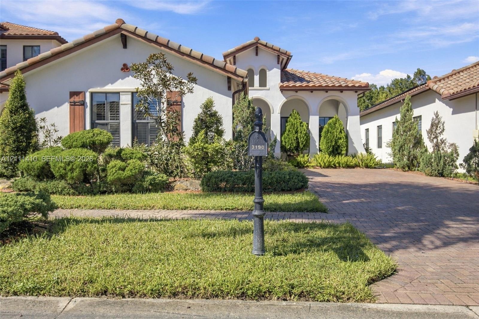 Stucco exterior with a clay tile roof, arched entryway, and paver driveway