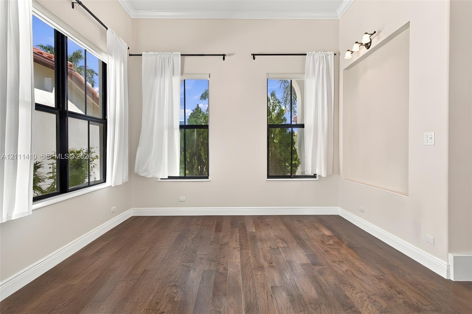 Room featuring dark wood-finish flooring, high ceilings with crown molding, black-framed windows, and a built-in recessed display niche with integrate