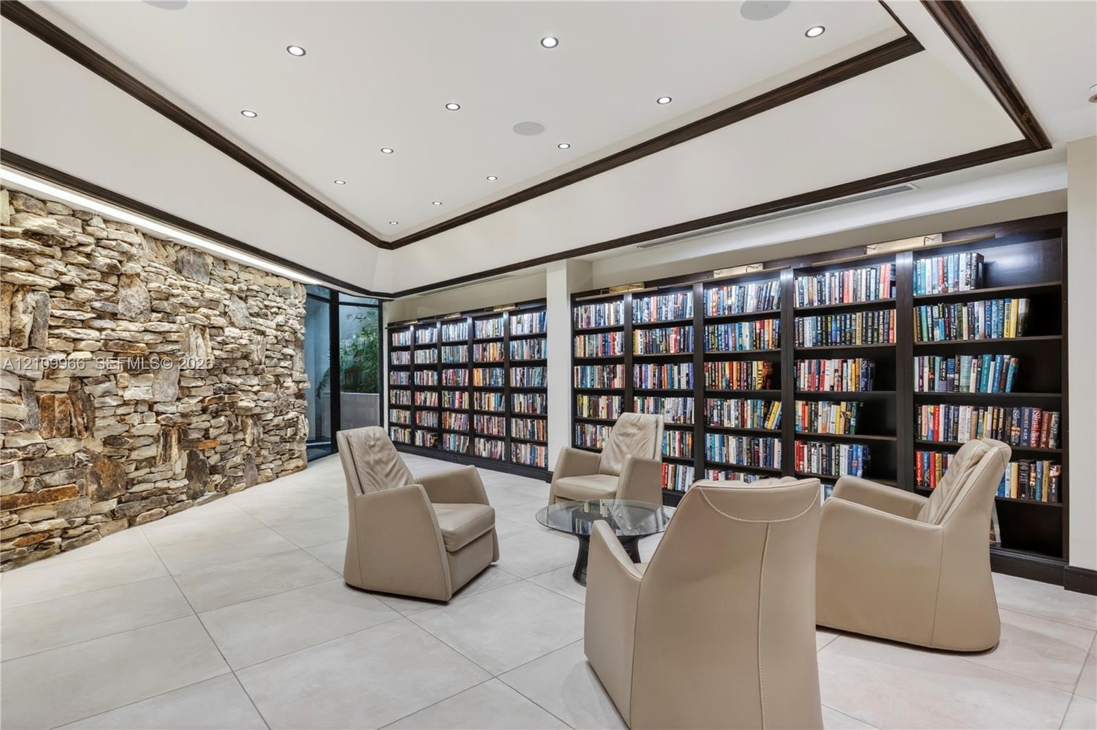 Floor-to-ceiling dry-stack stone accent wall, expansive built-in dark wood shelving, recessed lighting, and large-format tile flooring