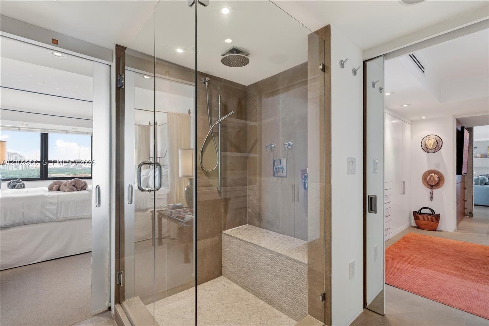 Walk-in glass-enclosed shower featuring a built-in stone bench, overhead rainfall showerhead, handheld sprayer, and neutral tile wall cladding