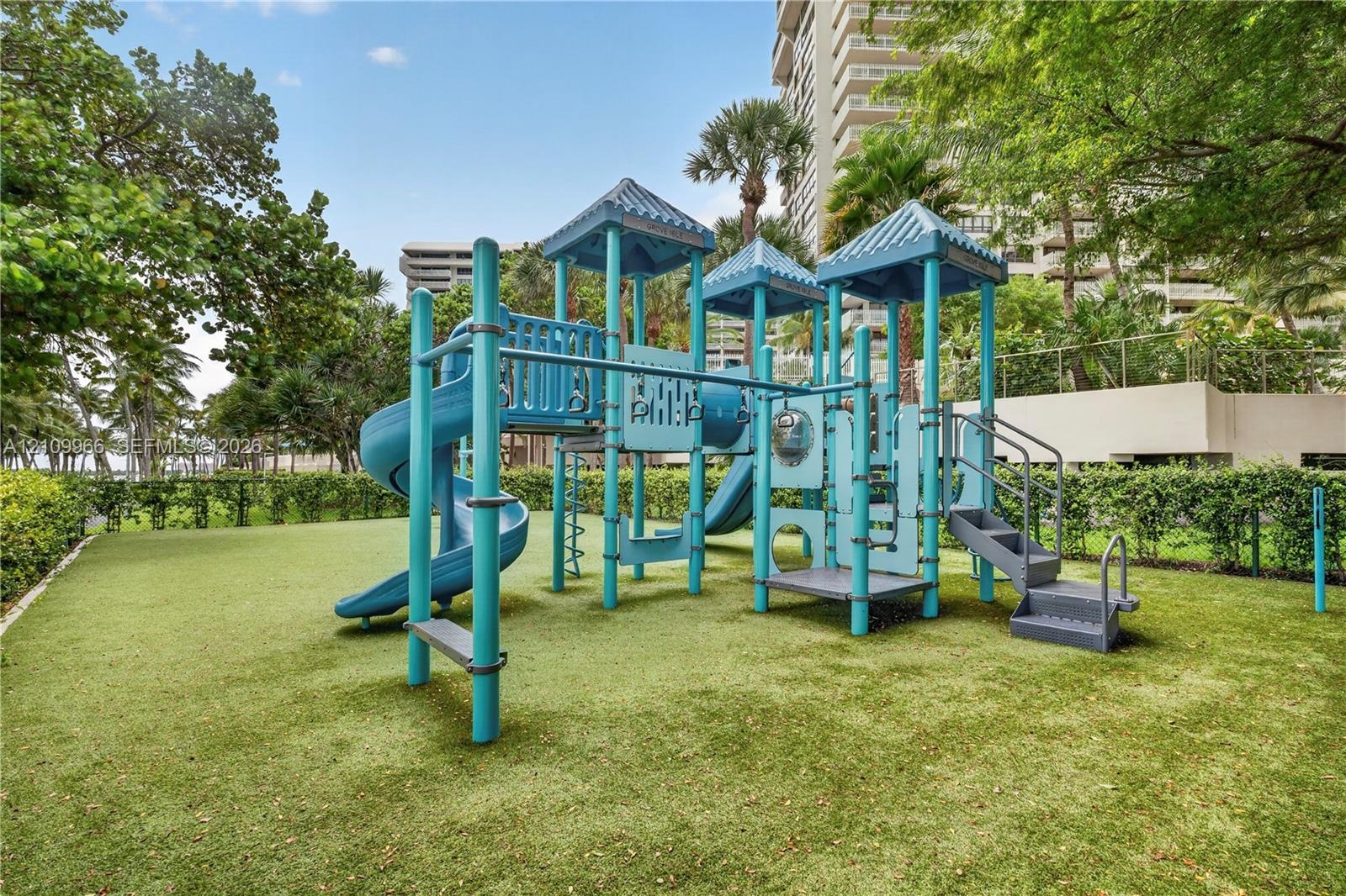 Recreational area featuring a multi-level climbing structure with integrated slides, stairs, and platforms situated on a manicured lawn enclosed by ma