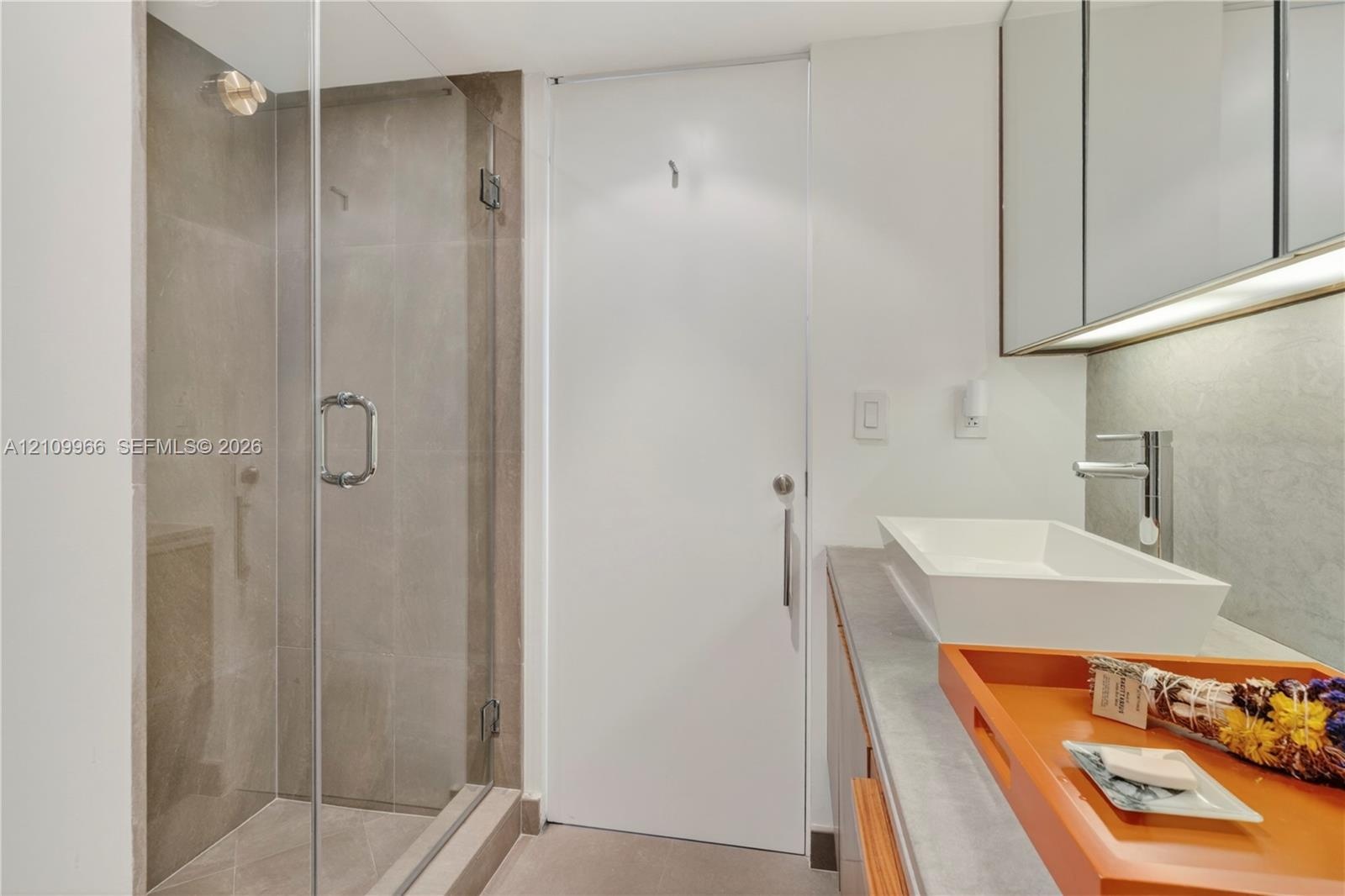Walk-in shower with frameless glass enclosure, rectangular vessel sink, polished chrome faucet, stone-finish countertop, and wall-mounted mirrored cab