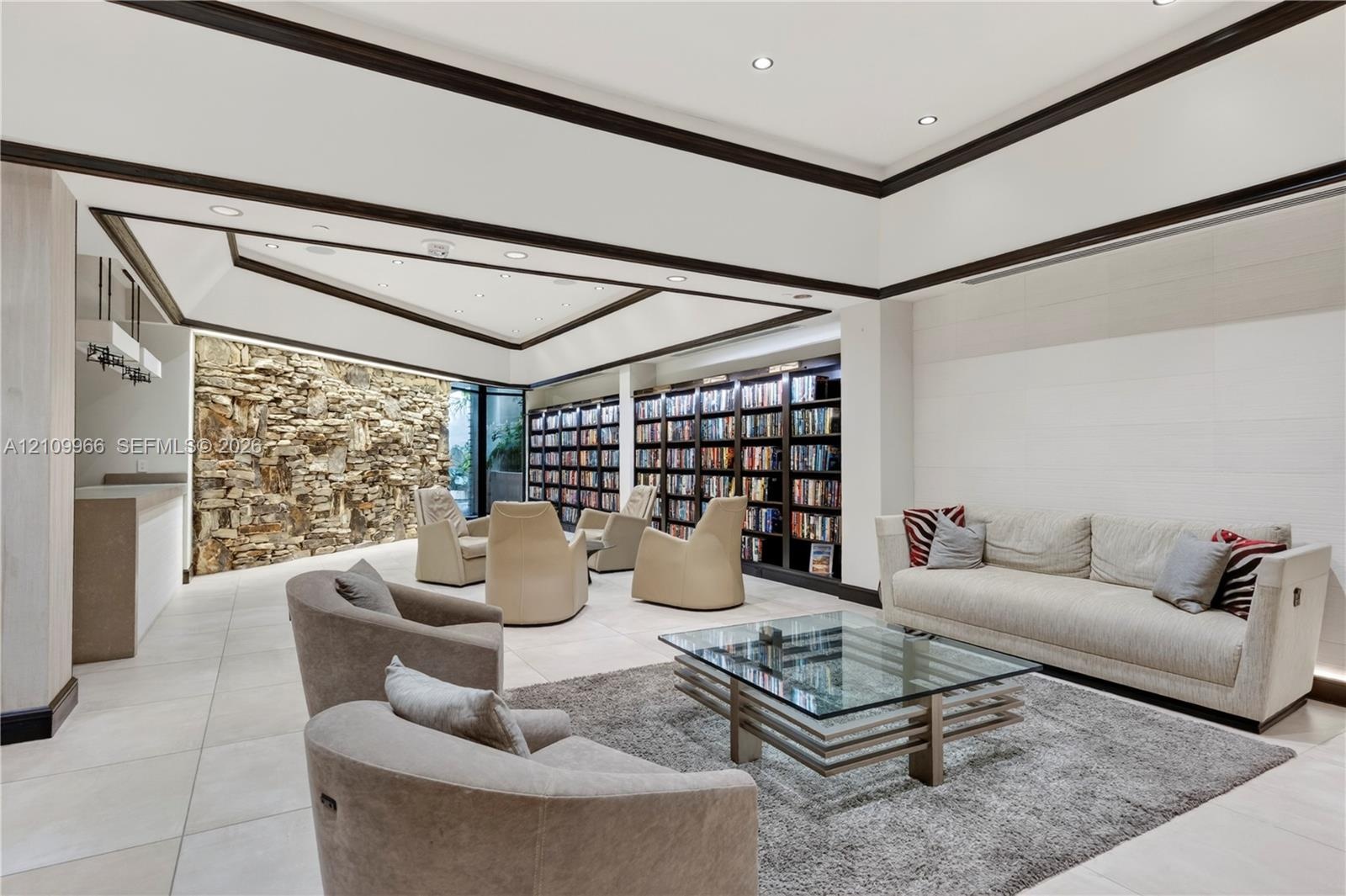 Spacious room featuring a tiered tray ceiling, large-scale stone accent wall, extensive built-in floor-to-ceiling shelving, recessed lighting, and lar