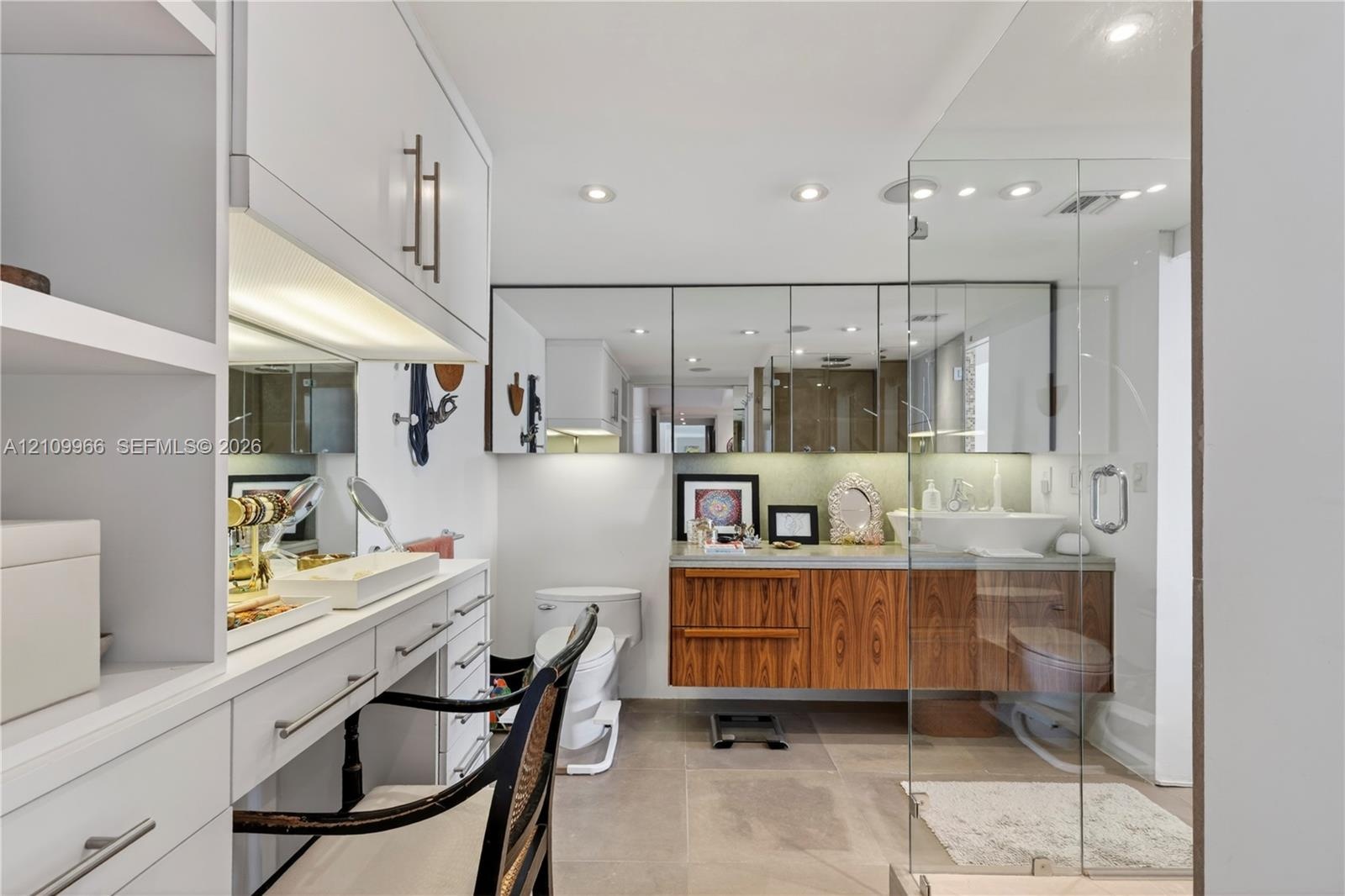 Wall-mounted wood-finish vanity with a rectangular vessel sink, integrated medicine cabinet mirrors, recessed lighting, and a glass-enclosed shower fe