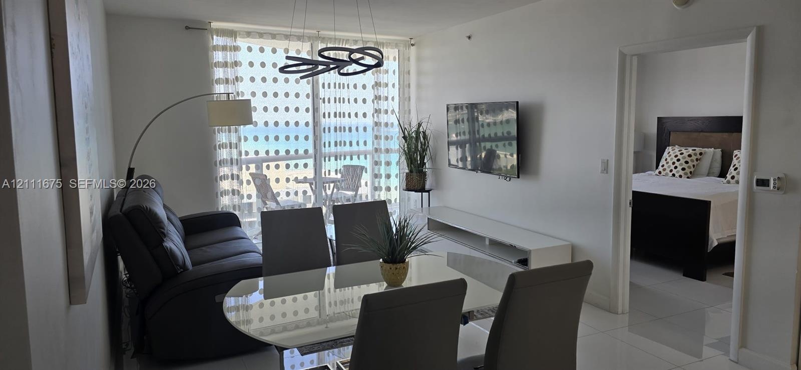 Living area featuring tile flooring, floor-to-ceiling glass sliding doors, modern circular pendant lighting, and an expansive balcony
