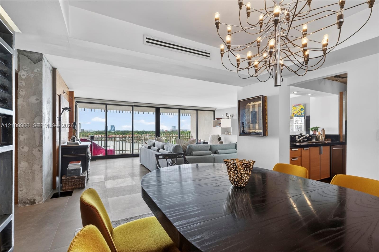 Open-concept interior featuring large-format tile flooring, exposed concrete structural column, floor-to-ceiling glass sliding doors, ornate metal cha