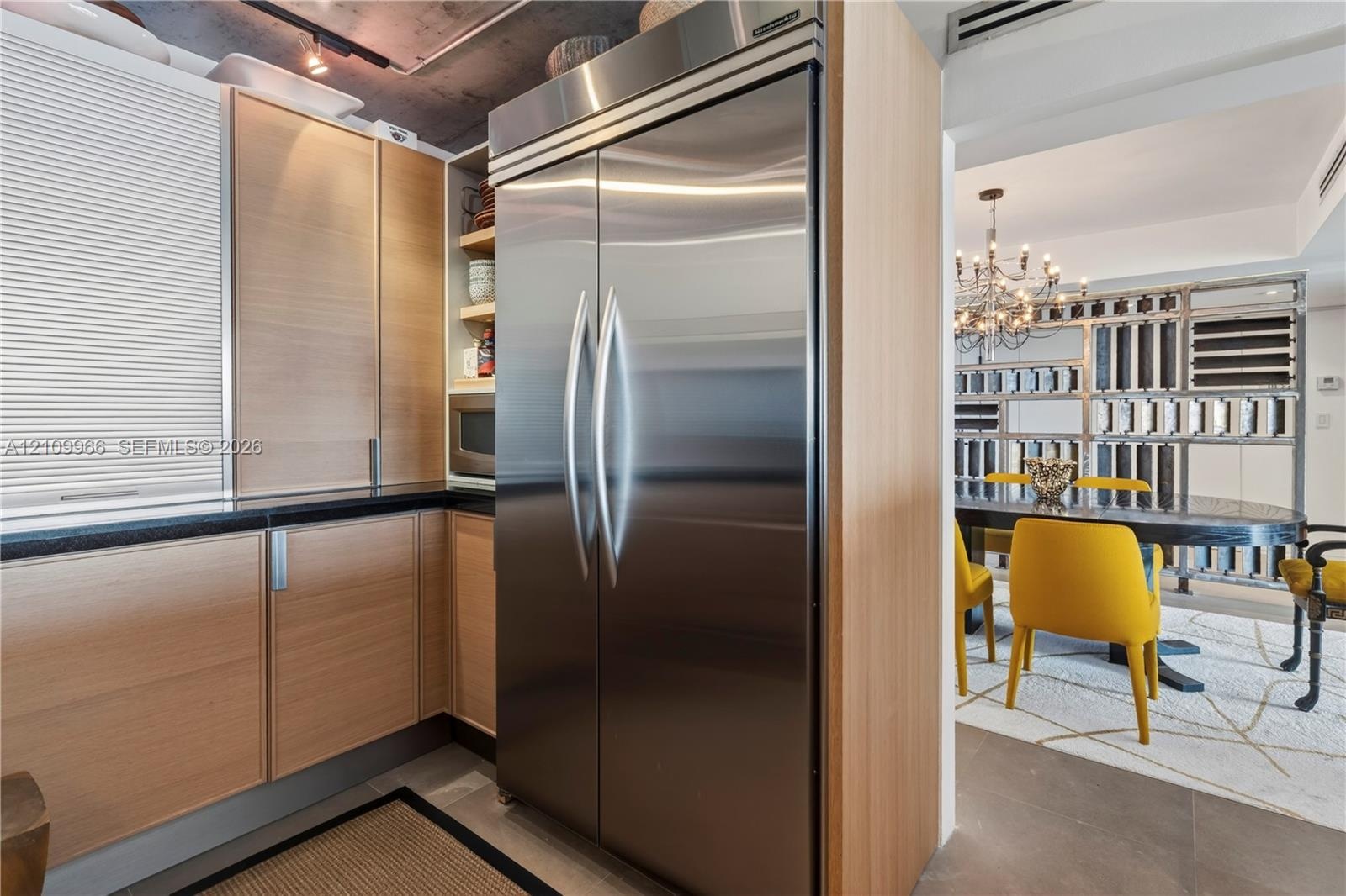 Kitchen featuring wood-veneer flat-panel cabinetry, professional-grade stainless steel refrigerator, black stone-composite countertops, and exposed co