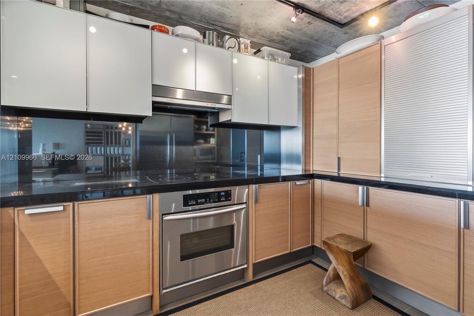 Kitchen featuring dual-toned flat-panel ceiling height cabinetry, dark stone countertops, integrated stainless steel oven, exposed concrete ceiling, a