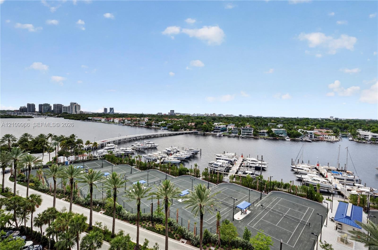 Waterfront property featuring a private marina with multiple boat slips and professional tennis courts surrounded by mature palm trees