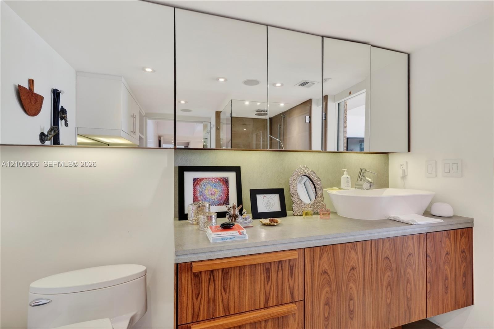 Floating vanity featuring wood-finish cabinetry, a stone-surface countertop, white vessel sink, and an expansive wall-to-wall mirrored medicine cabine