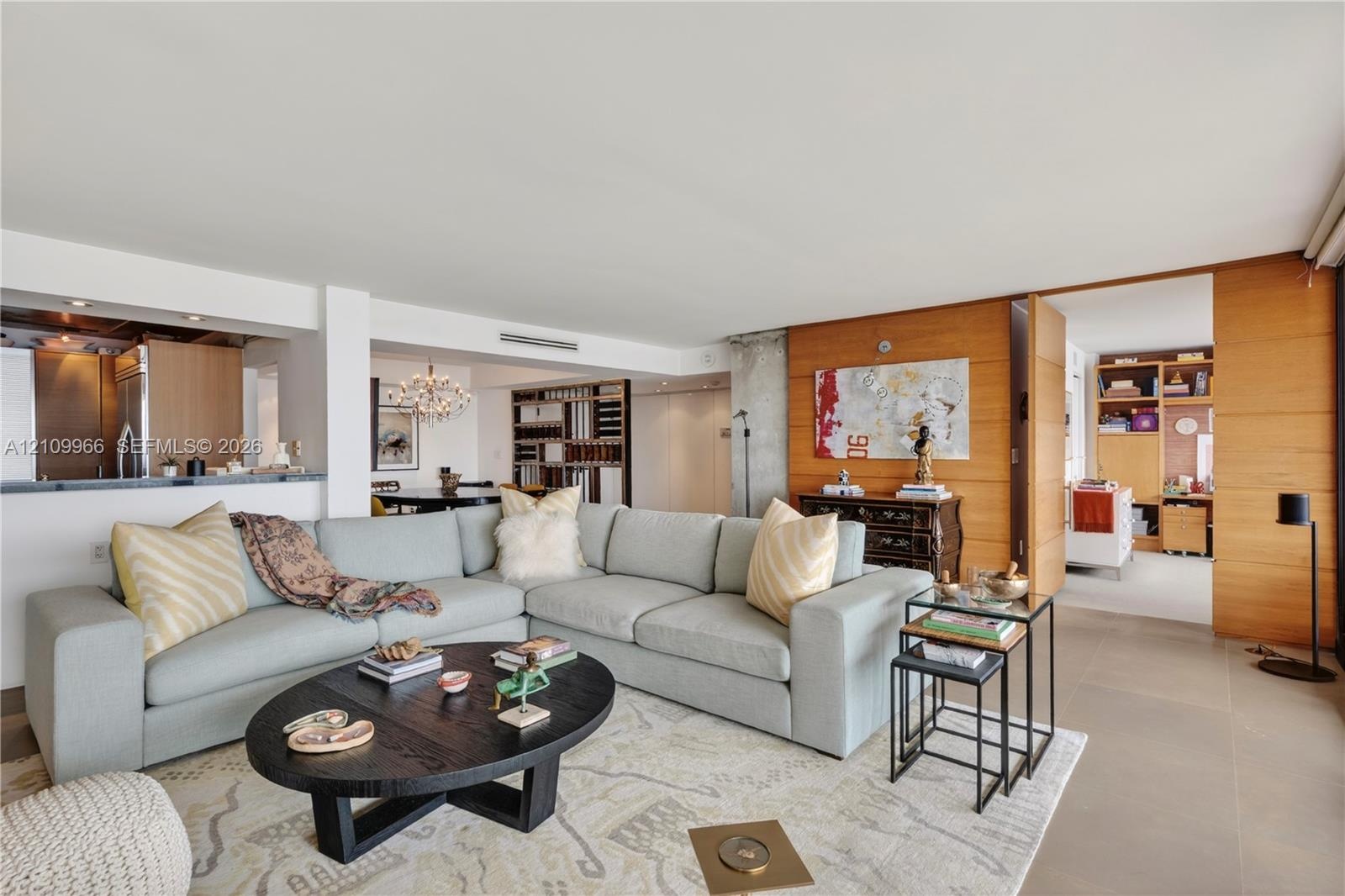 Open-concept living space featuring wood-paneled walls, large-format tile flooring, a concrete structural pillar, and built-in shelving