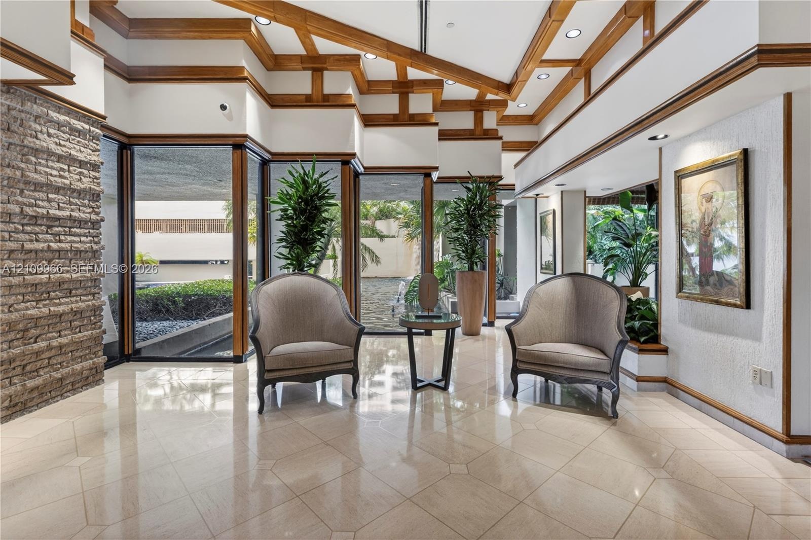 Vaulted ceiling with exposed wood-beam detailing, polished stone tile flooring, expansive floor-to-ceiling windows, and integrated stone masonry accen