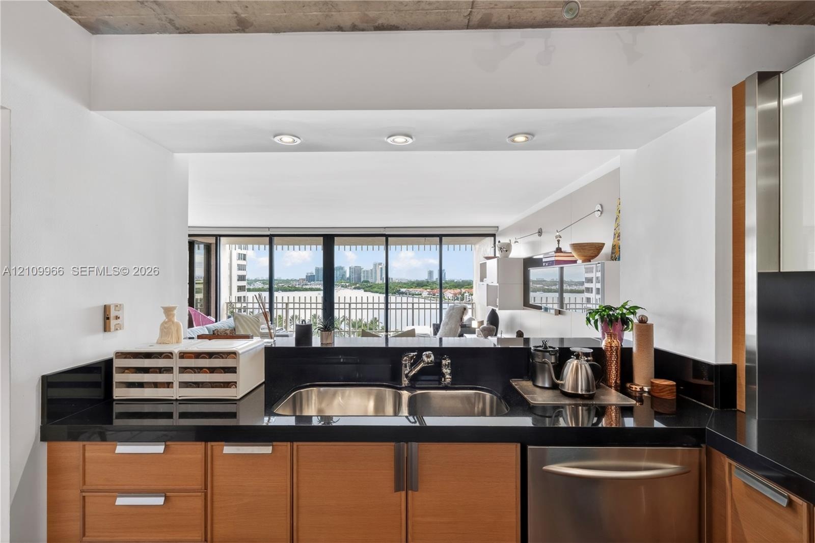 Kitchen featuring wood cabinetry, black solid-surface countertops, dual-basin stainless steel sink with a high-arch faucet, stainless steel dishwasher