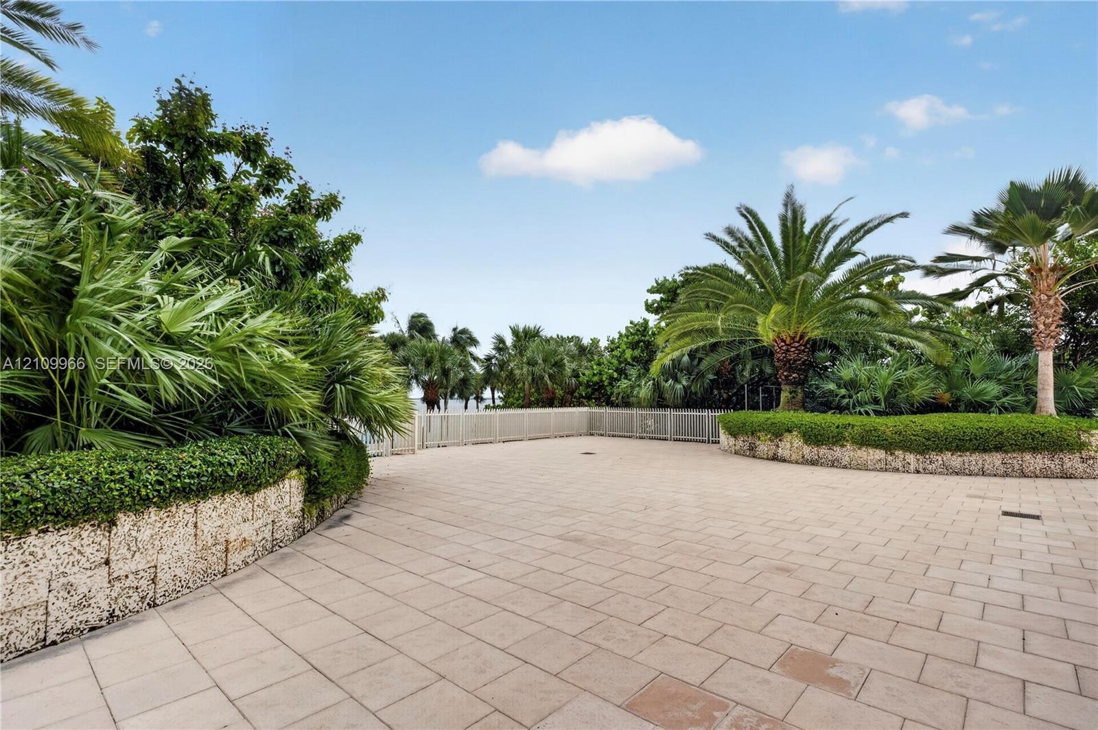 Outdoor terrace featuring oversized stone-style pavers, tiered natural stone retaining walls, and mature palm landscaping with a metal perimeter fence