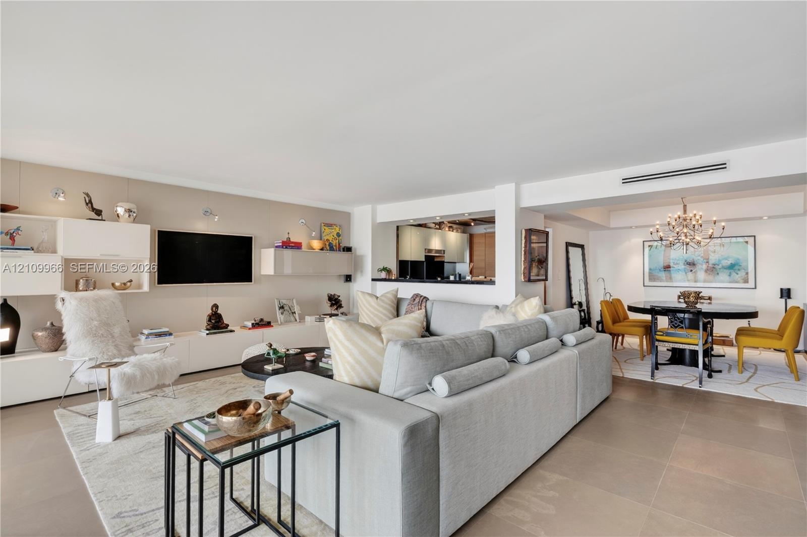 Open-concept interior featuring large-format tile flooring, built-in high-gloss cabinetry, recessed accent lighting, and a multi-tiered crystal chande